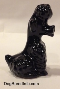 The right side of a figurine of a black Poodle sitting. The figurine has a small tail.