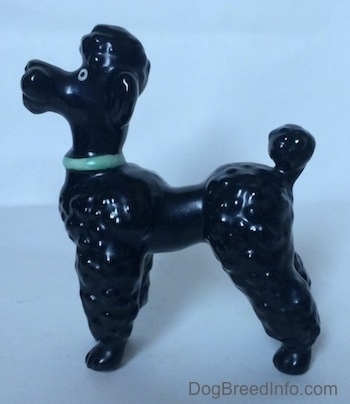 The left side of a black Poodle figurine with a green collar. The figurine has hair poofs all over its legs.