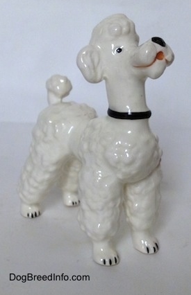 The front right side of a white Poodle figurine. The figurine has black circles for eyes.