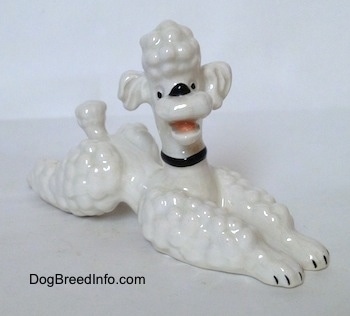 The front right side of a white Poodle in a lying pose figurine. The figurines mouth is open.
