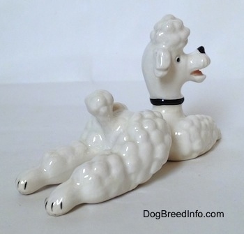 The back right side of a white Poodle figurine in a lying Pose. The figurine has its mouth open and its head turned to the right.