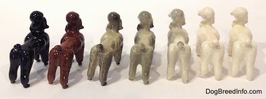 The back of seven different color variations of a Poodle standing figurine. It is hard to differentiate the ears of the figurines from the heads.