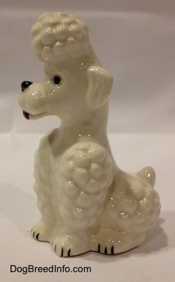 The left side of a white figurine of a Poodle in a sitting pose. The figurine has poofy haired legs.