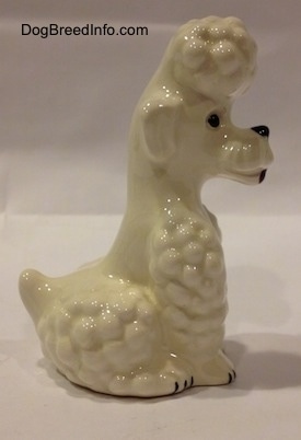 The right side of a figurine of a white Poodle in a sitting pose figurine. It is hard to differentiate the ears of the figurine from its head.