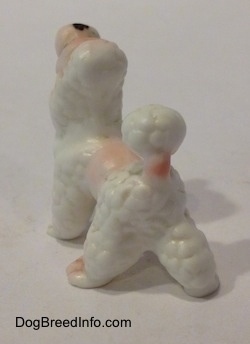 The back left side of a figurine of a bone china Poodle puppy figurine. The figurine has pink spots across its body.