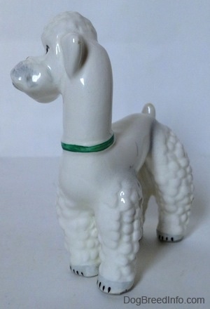 The front left side of a white Poodle with a green collar on figurine. The figurine has black tipped nails.