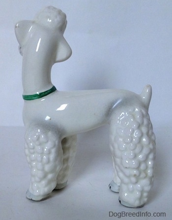 The left side of a white Poodle figurine that has a green collar. The figurine has a small tail that is sticking up.