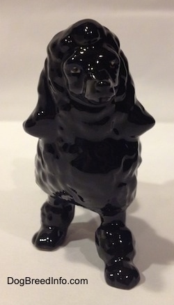 A figurine of a black porcelain Poodle. The figurine has hair poofs going down its legs.