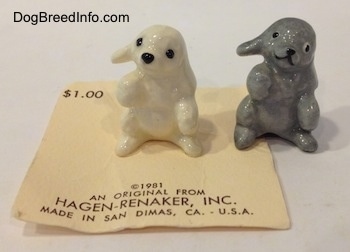 A gray and a white version of a figurine of Poodle puppy in a begging pose.