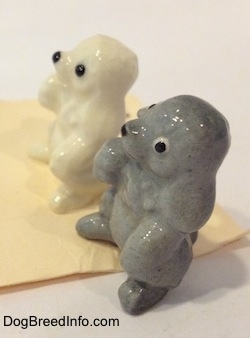 The left side of two different color variations of a Poodle puppy in a begging pose. The ears of the figurines are hard to differentiate from the head.
