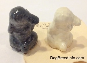 The back of two different color variations of figurines of a Poodle puppy in a begging pose. The tails of the figurines are short and hard to differentiate from the body.