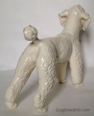 The back right side of a white figurine of a Poodle. The figurine has a small poofy tail.