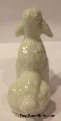 The back of a white bone china figurine of a Poodle in a seated position. The figurine has a small poofy tail.