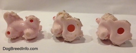 The underside of three pink porcelain spaghetti Poodle puppy figurines.
