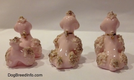 The back of three figurines of pink porcelain spaghetti Poodle puppies. The figurines are all wearing three gold collars.
