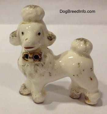 The left side of a porcelain Poodle figurine. The figurine has small black circles for eyes.
