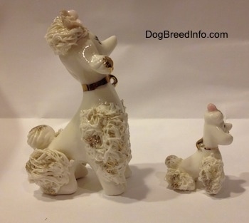 The right side of two figurines of white spaghetti porcelain Poodles. The figurines are wearing gold collars.