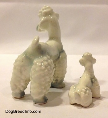 The back right side of two white Poodle figurines with spots of gray. The figurines tails are short and arched in the air.