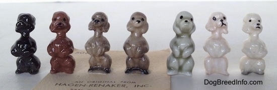 A line-up of seven different color variations of a Poodle puppy in a begging pose figurine.