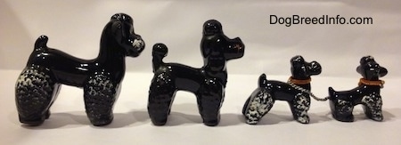 The right side of four black clay Poodle figurines. The front two figurines are chained together and wearing red chains.