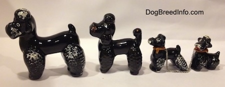The right side of four figurines of black clay Poodles. Thefront figurine has a large white circle with a black circle in the middle.