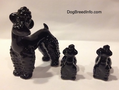 There are two black Poodle puppy figurines next to a large black Poodle figurine.