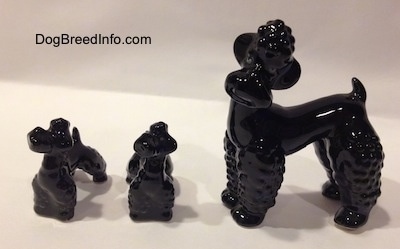 The left side of a black Poodle figurine and to the left of it is two black Poodle figurine puppies.