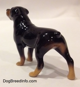 The back left side of a brown with black miniature Rottweiler figurine. The figurine is glossy.