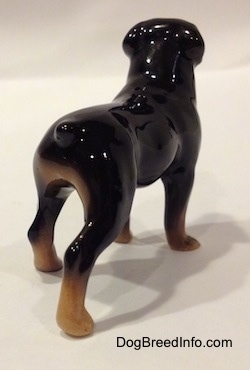 The back right side of a brown with black miniature figurine of a Rottweiler. The figurine has a small tail.