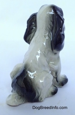 The back left side of a figurine of a white with black figurine. The figurine is glossy.