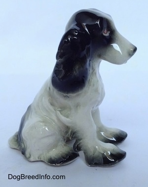 The right side of a figurine of a white with black Russian Spaniel dog sitting. The end of the figurines paws are black.
