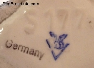 Close up - The underside of a Russian Spaniel dog stein cup. There is two stamps and an engraving on the underside. There is a blue stamp of the full bee inside the V logo of Goebel W.Germany and then the black stamp of Germany. The engraving above the stamps reads 'S177'.