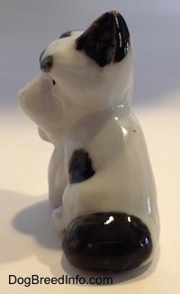 The back of a white with black bone china Schnauzer sitting figurine. The figurine has a large black spot above its tail.