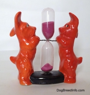 Two orange figurines of miniature Schnauzers standing on their hind legs. They both have black circles inside of white circles for eyes.