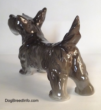 The back left side of a black, grey and white miniature Schnauzer figurine. The figurine has its ruffled tail arched into the air.