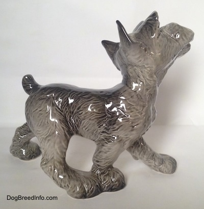 The right side of a figurine of a grey with white Schnauzer puppy. The figurine is of a Schnauzer walking.
