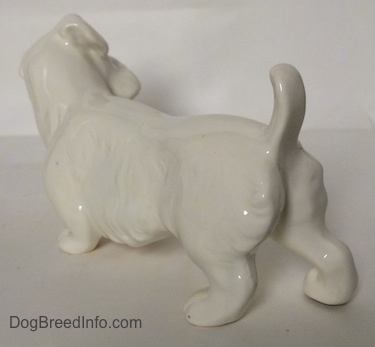 The back left side of an unpainted figurine of a white Sealyham Terrier. The figurine has its tail arched in the air.