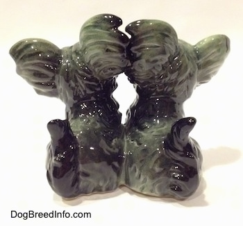The back of a gray and black figurine of Siamese twin Skye Terriers sitting. The tails of the figurines are short and arched in the air.