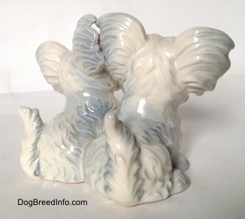 The back right side of a figurine of a silver platinum Siamese twin sitting Skye Terrier. The figurines are glossy.