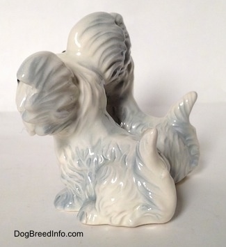 The left side of a Siamese twim silver platinum figurine of a Skye Terrier sitting. The white tails of the figurines are in the air.