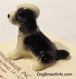 The back left side of a black with white English Springer Spaniel figurine in a sitting position. The figurine has a short black tail.