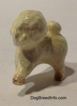 The front left side of a white with brown walking Toy Poodle figurine. The ears of the figurine are hard to differentiate from the head.
