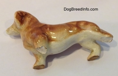 The underside of a tan ceramic Dachshund figurine with two broken legs. The figurine has a long body.
