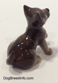 The back left side of a Wolf cub sitting figurine. The figurine has short ears that are in the air.